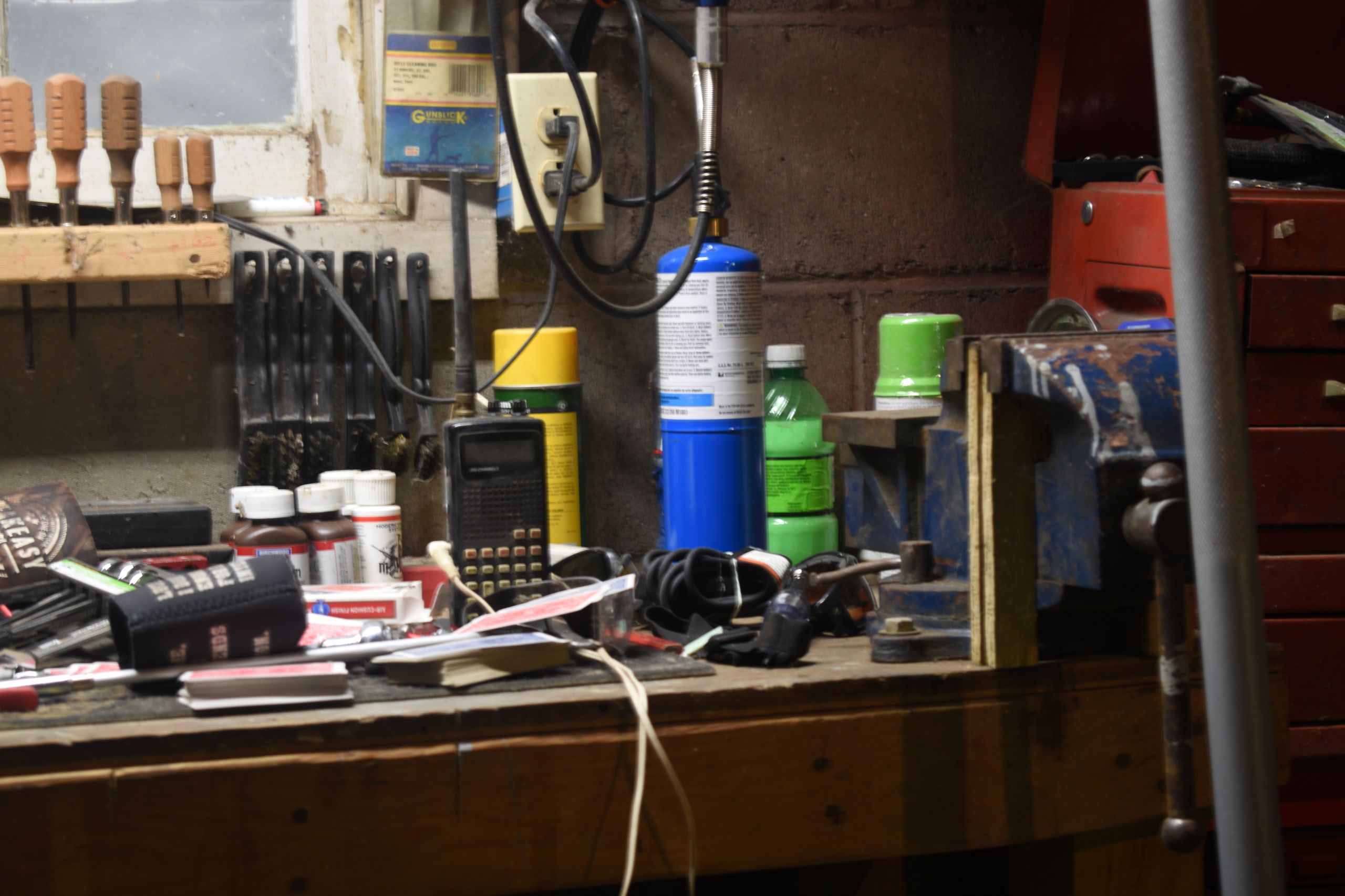 Cluttered garage workbench with hand tools, a bench vise, radio, and small engine supplies.