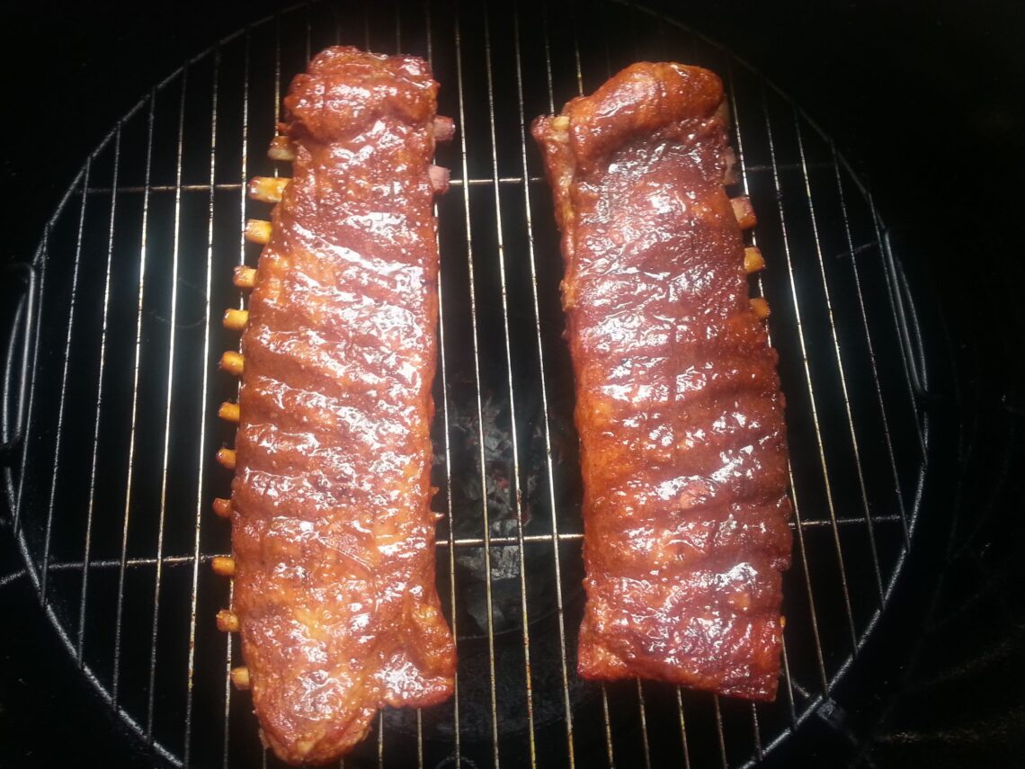 Two racks of pork ribs cooking on an Ugly Drum Smoker grill grate.