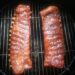 Two racks of pork ribs cooking on an Ugly Drum Smoker grill grate.
