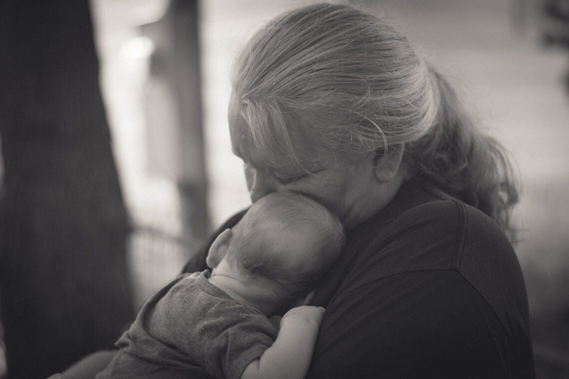 Monochrome photo of a woman holding her three-year-old grandson tightly against her chest outdoors during a summer cookout.
